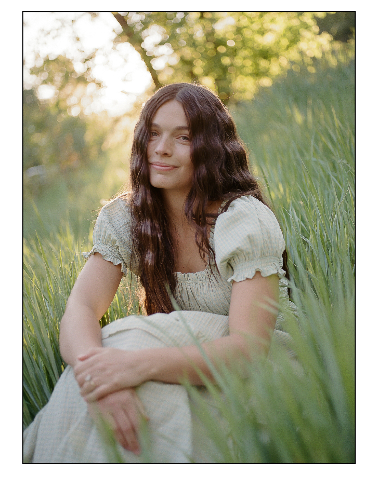 Shelby, founder of Ryze, in a sage gingham dress sitting in tall sunlit grass at golden hour